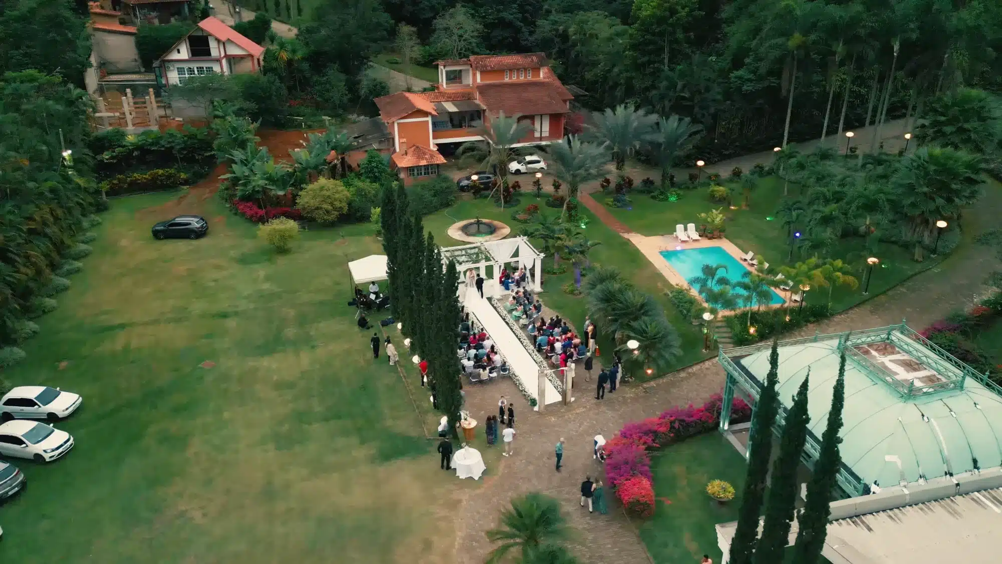 Cerimônia de casamento ao ar livre no Sposato, em Leopoldina, vista de drone: caramanchão branco, jardim com fonte, piscina e mata ao redor